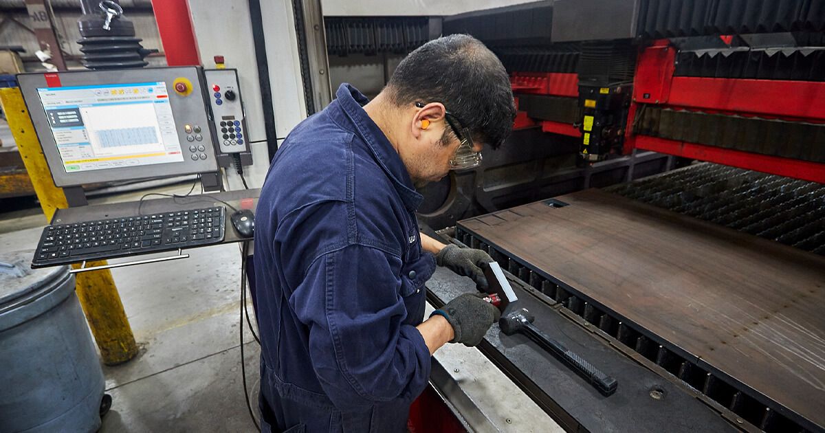Metal fabricator measuring metal part in front of laser cutting machine.